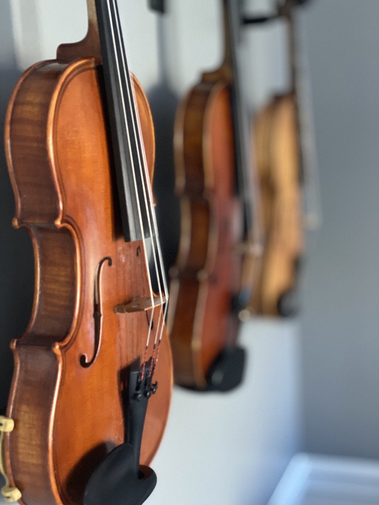 Three violins hanging on a wall, side by side.